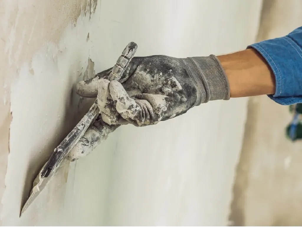 Professional applying compound to a wall with a putty knife, illustrating the importance of proper preparation before painting.