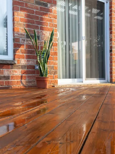 Beautifully restored wooden deck with a glossy finish, set against a brick house exterior, showcasing Bay Breeze Painting Company's deck restoration services.